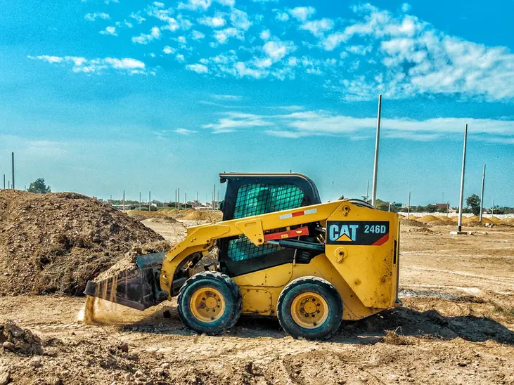 A compact track loader working a graded dirt pad on a clear day