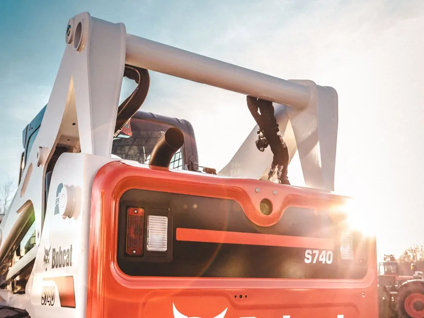 A compact skid steer loader with the bucket down, parked ready to load debris