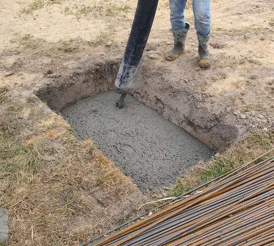 Concrete being placed into a small excavated section with reinforcing bar to one side