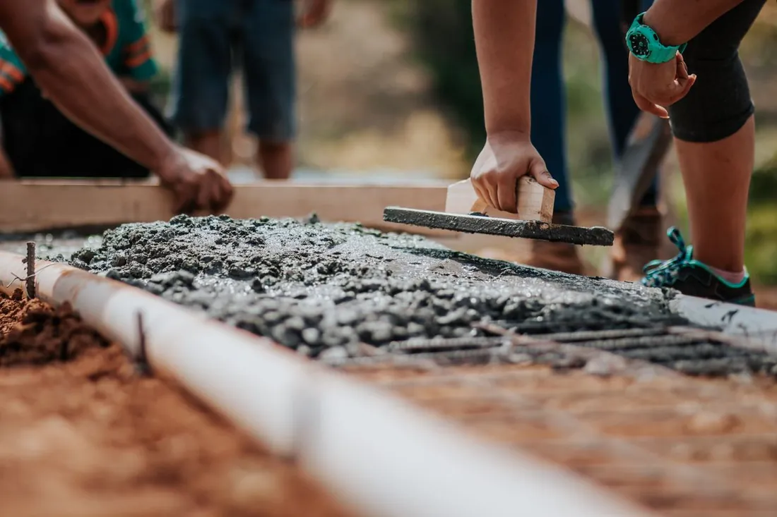 Hands working fresh concrete into a formed edge with a hand float