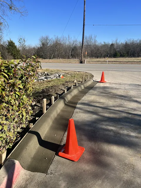 A new concrete curb set along a roadway, coned off