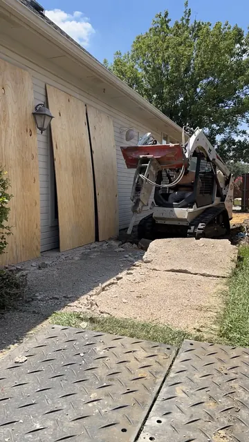 A skid steer breaking out old concrete beside a home