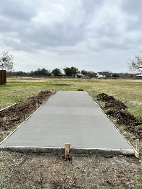 A long new concrete driveway run across an open lot