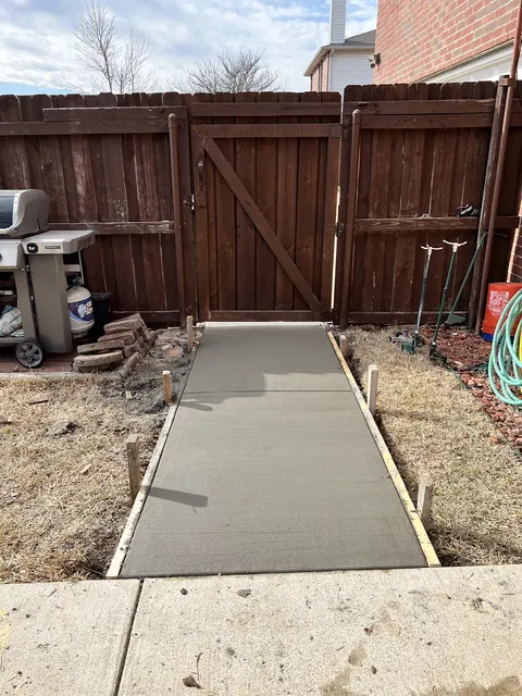 A freshly poured walkway between the fence and the house