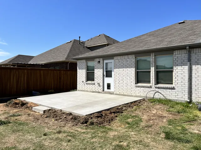 A new concrete patio slab behind a white brick home