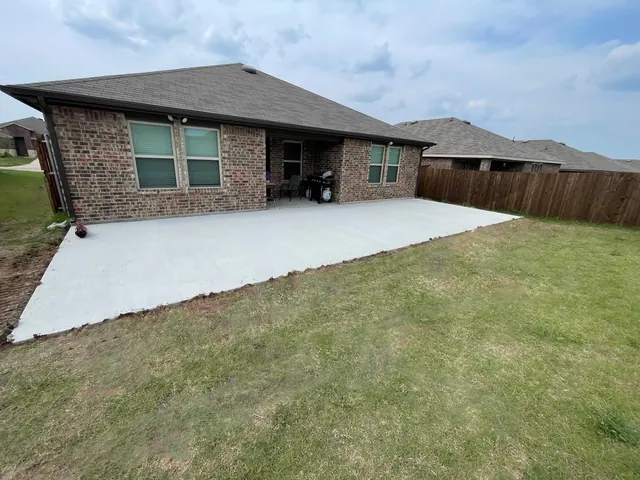 A wide new concrete patio across the back of a brick home